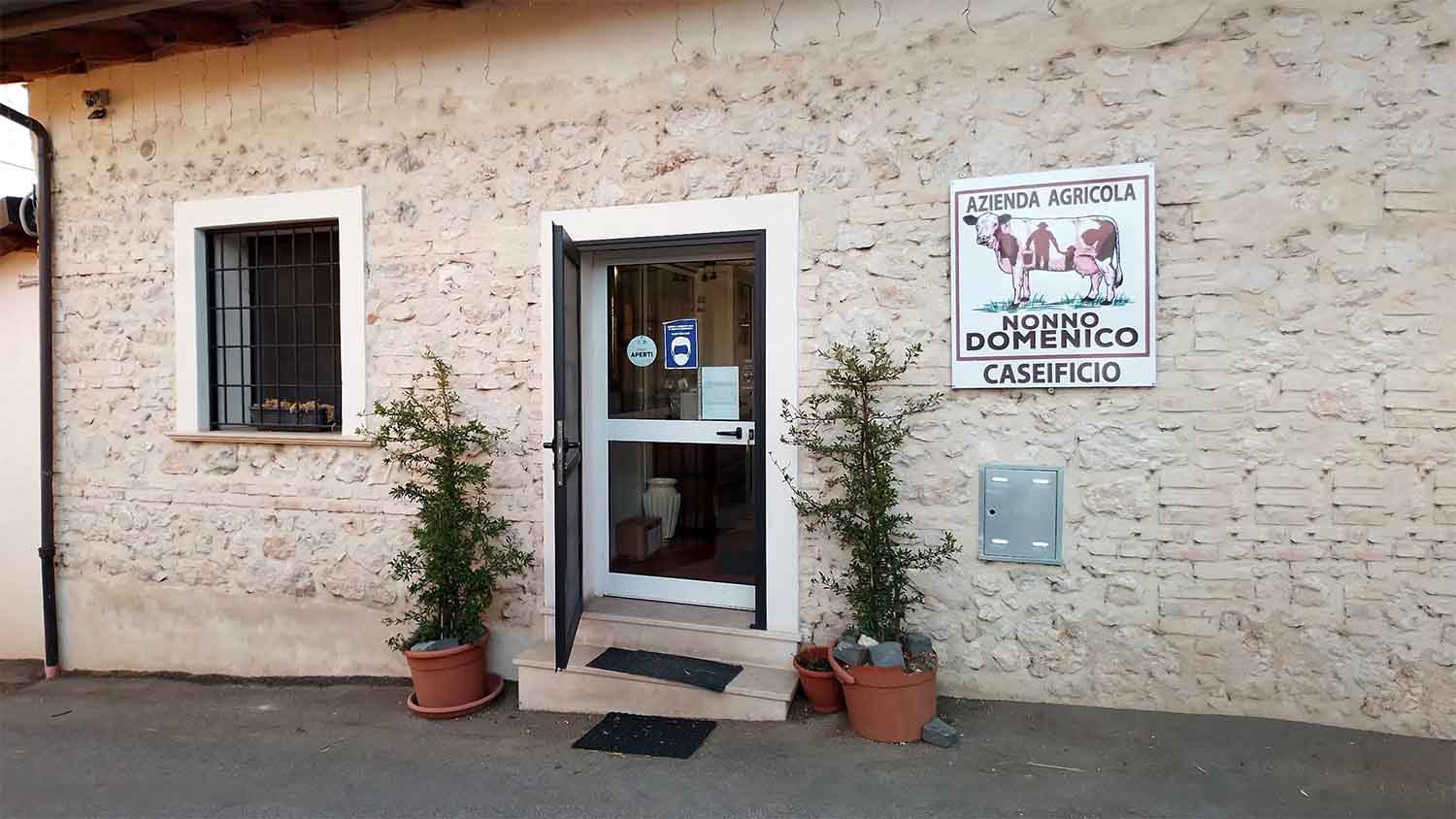 The entrance to Caseificio Nonno Domenico, an azienda agricola in Forme, Abruzzo, Italy, with a hand-painted farm sign and potted plants flanking the door