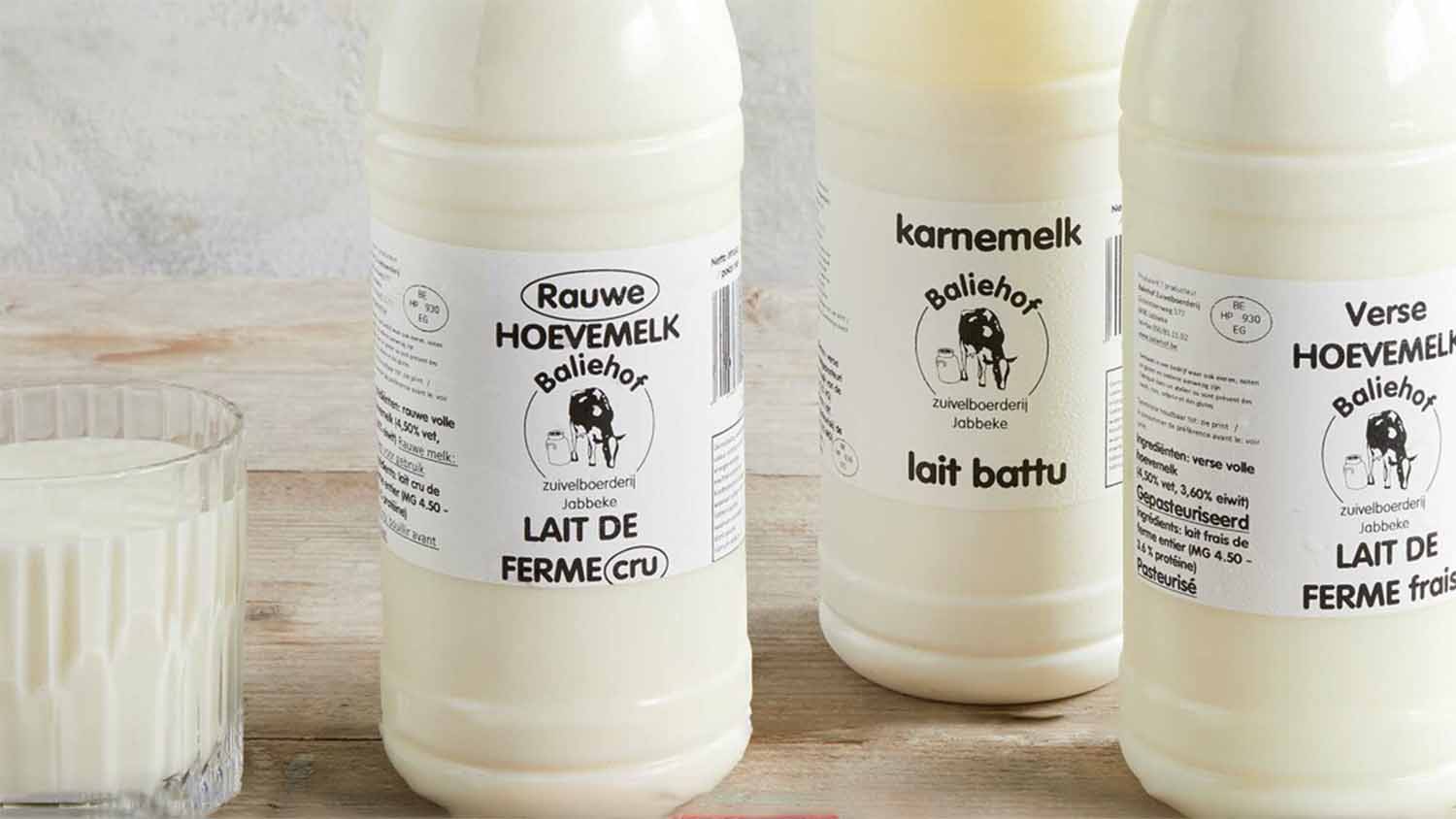 Three bottles from Baliehof zuivelboerderij in Jabbeke, Belgium, with bilingual Dutch and French labels: Rauwe Hoevemelk and Lait de Ferme cru on the left, karnemelk and lait battu in the centre, and a glass of milk alongside