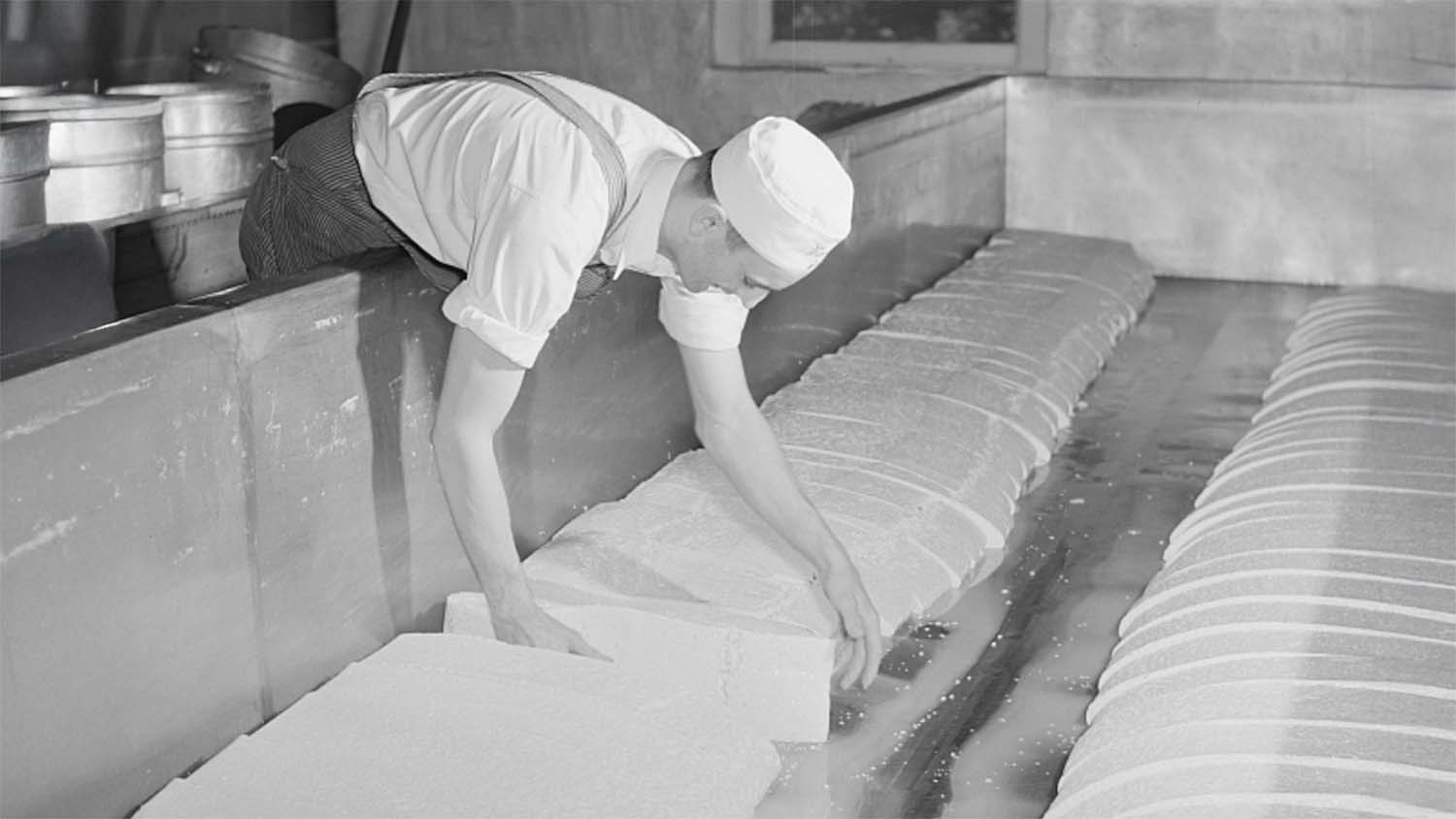 Cheesemaker Arvid Grimstead working cheddar curd in an open vat at the cooperative creamery in Westby, Wisconsin, circa 1941, photographed for the U.S. Farm Security Administration.