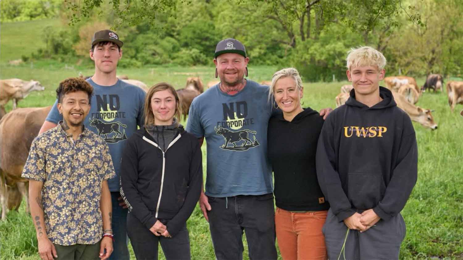 Grassway Organics farm team standing in a green pasture with grazing Jersey cows at the East Troy, Wisconsin raw milk dairy.