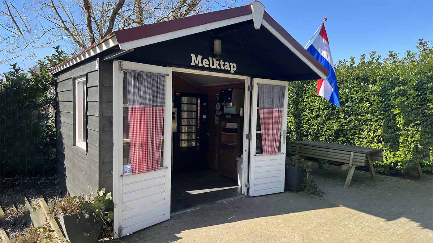 Melktap kiosk at Melkveehouderij Van Gastel dairy farm in Rucphen, North Brabant, Netherlands, a small wooden hut with the word Melktap above the door and a Dutch flag
