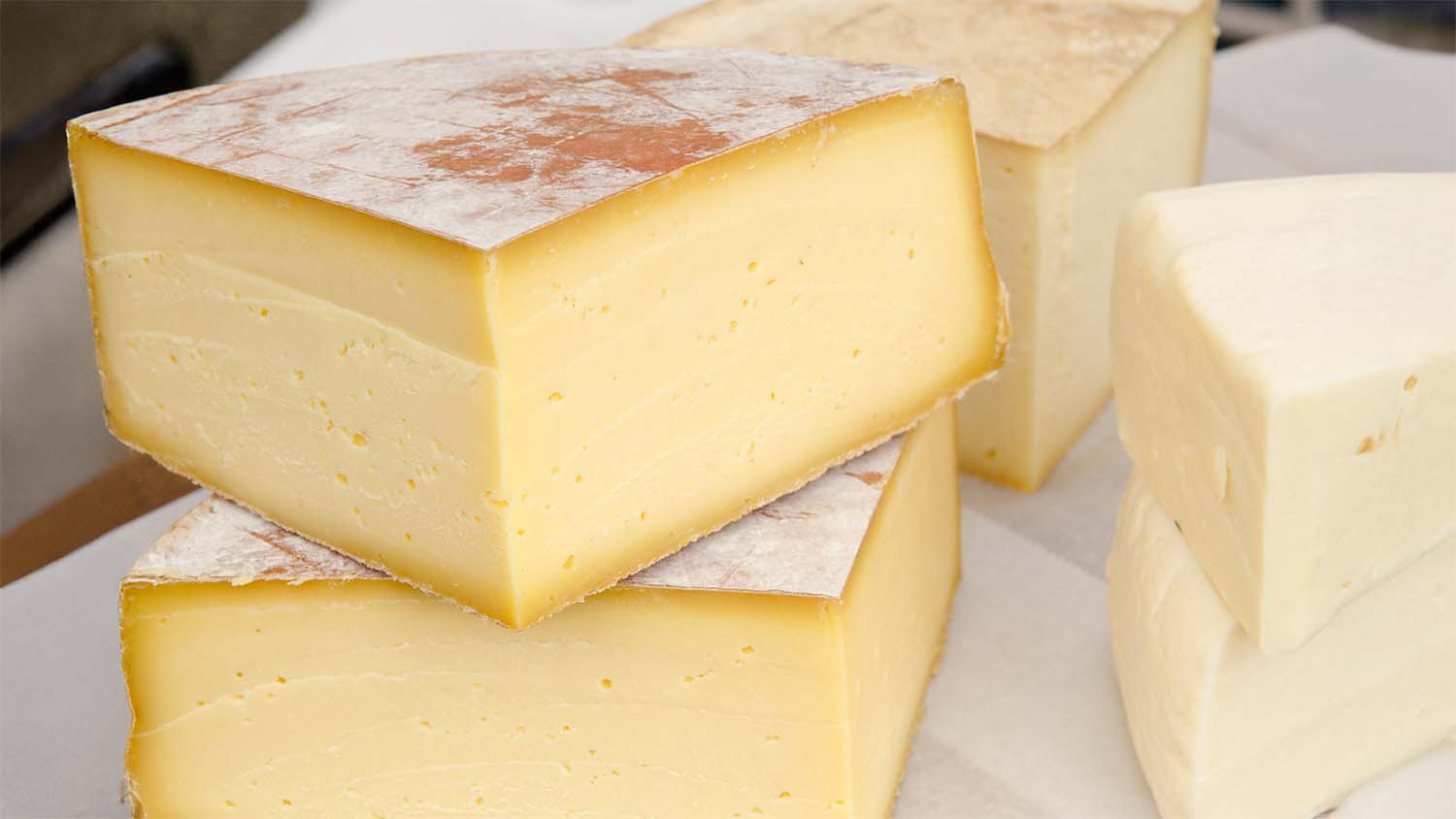 Wedges of natural-rind aged cheese displayed at a USDA farmers market, showing the firm texture and pale interior typical of hard aged styles.